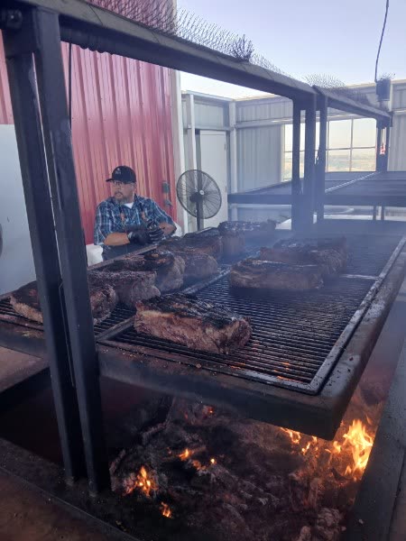 Un cocinero voltea los cortes de tri-tip sobre las brasas de roble.