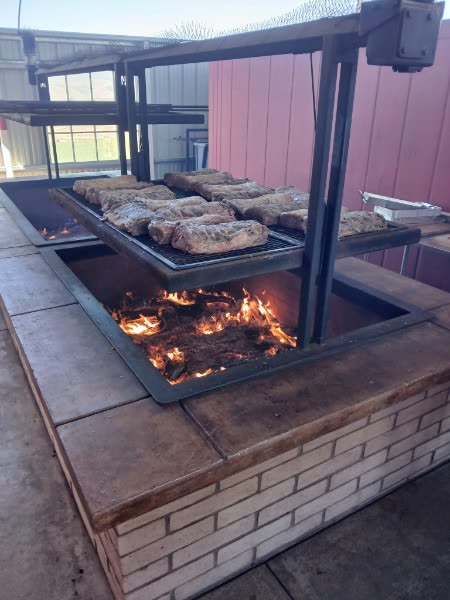 Tri-tip asándose sobre fuego abierto de leña de roble en la parrilla ajustable del rancho.