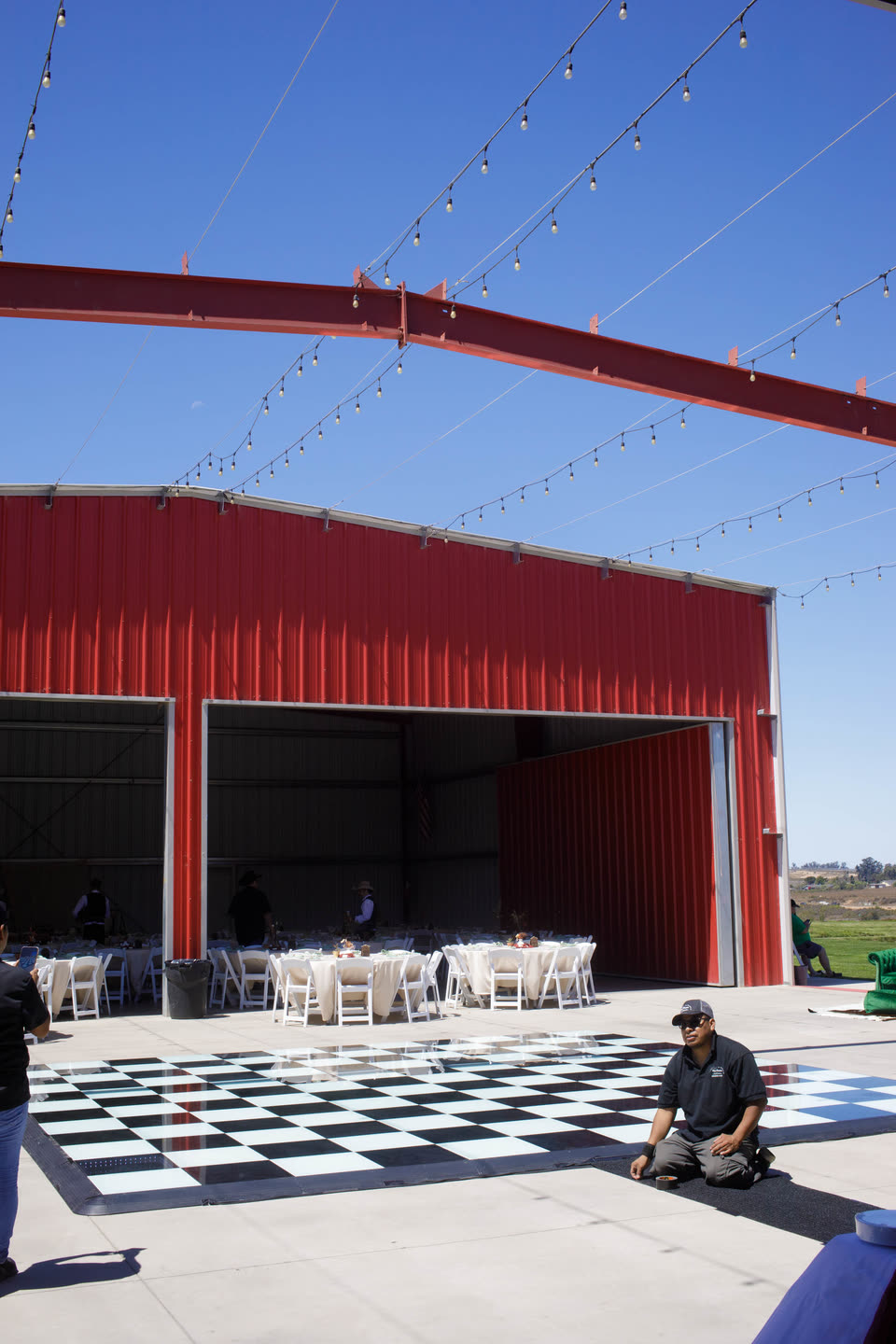 The red event barn with its bay doors open, string lights overhead and a black-and-white checkered dance floor laid out on the patio.